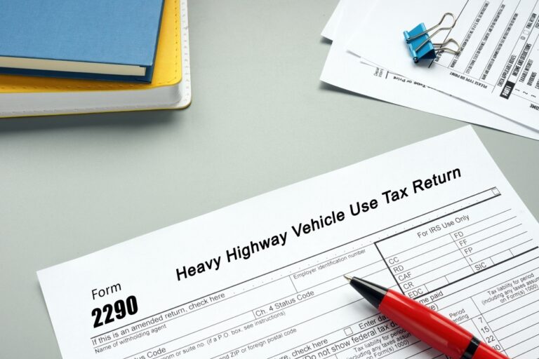 IRS Form 2290 and red pen on a desk, indicating the importance of adhering to the filing deadline for heavy highway vehicle use tax.